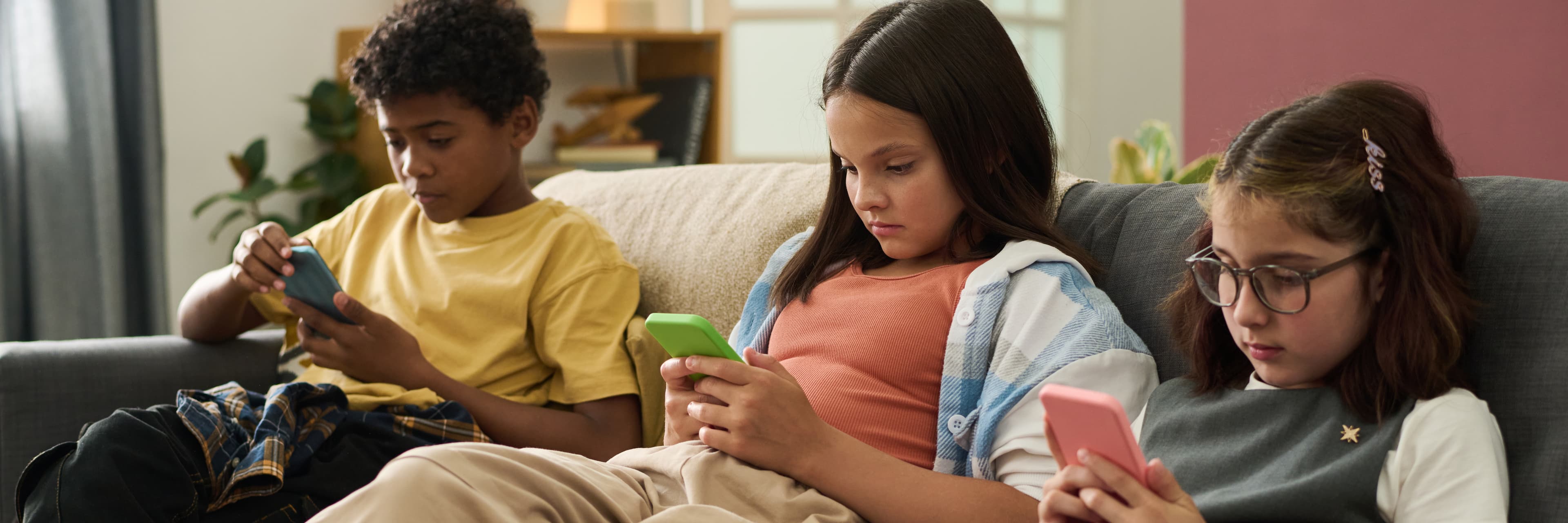 Three children sitting together, each absorbed in their own phone
