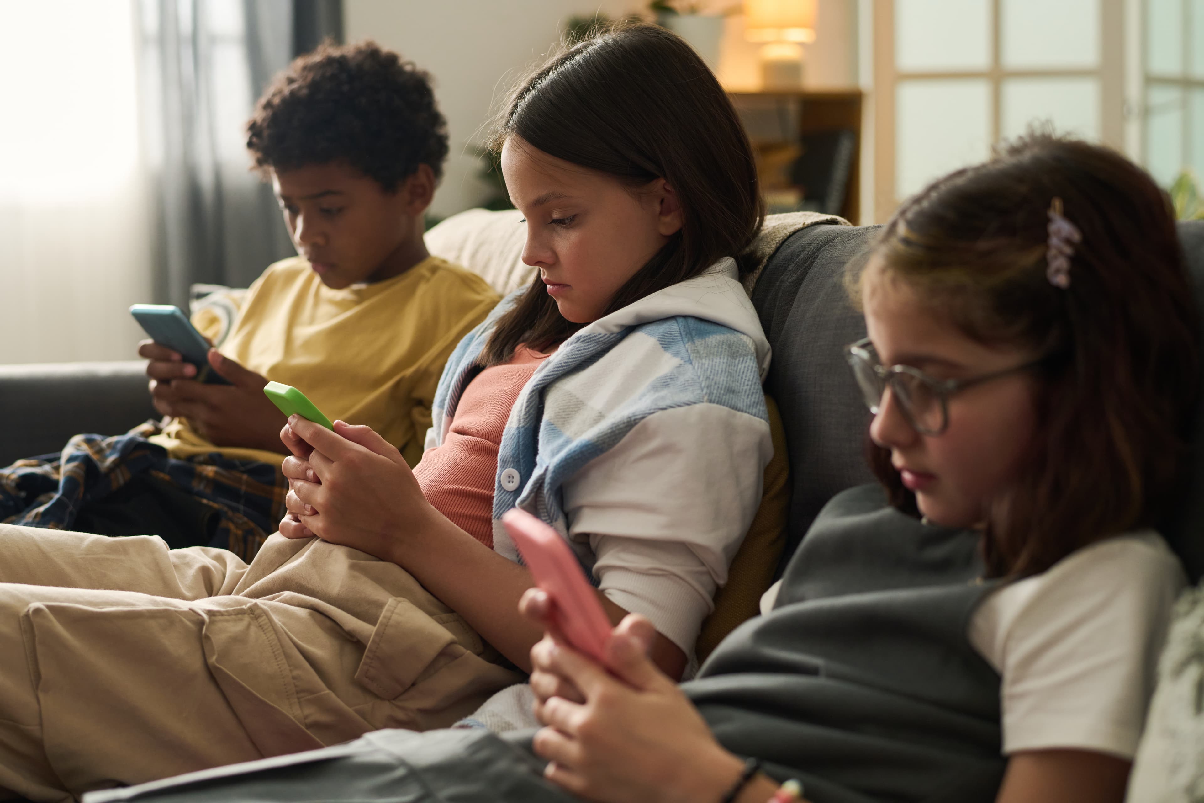 Three children sitting together each absorbed in their own phone