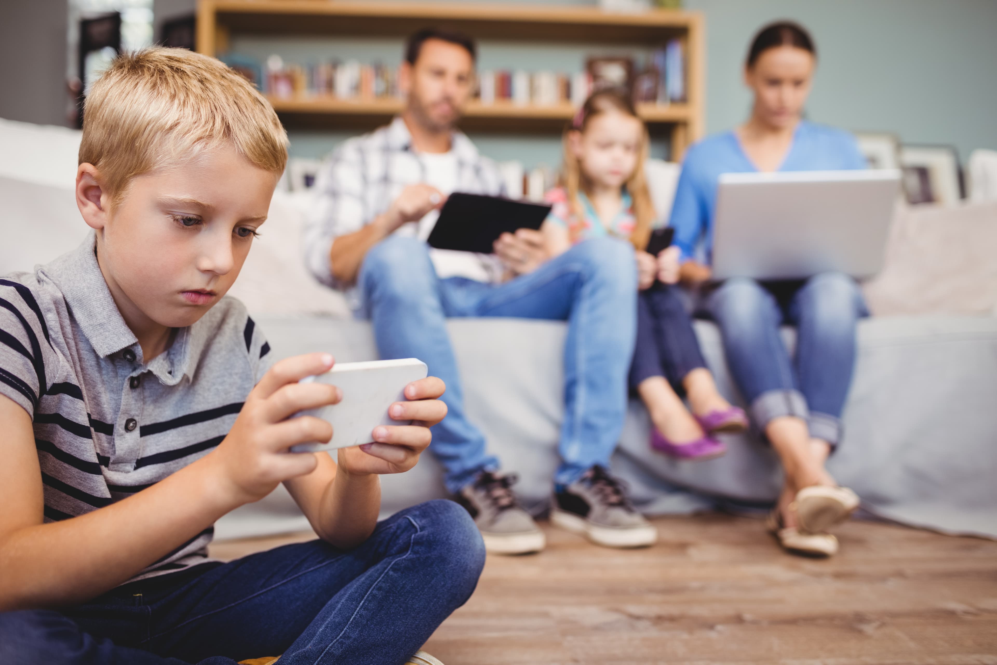 Family sitting in a living room each absorbed in separate devices