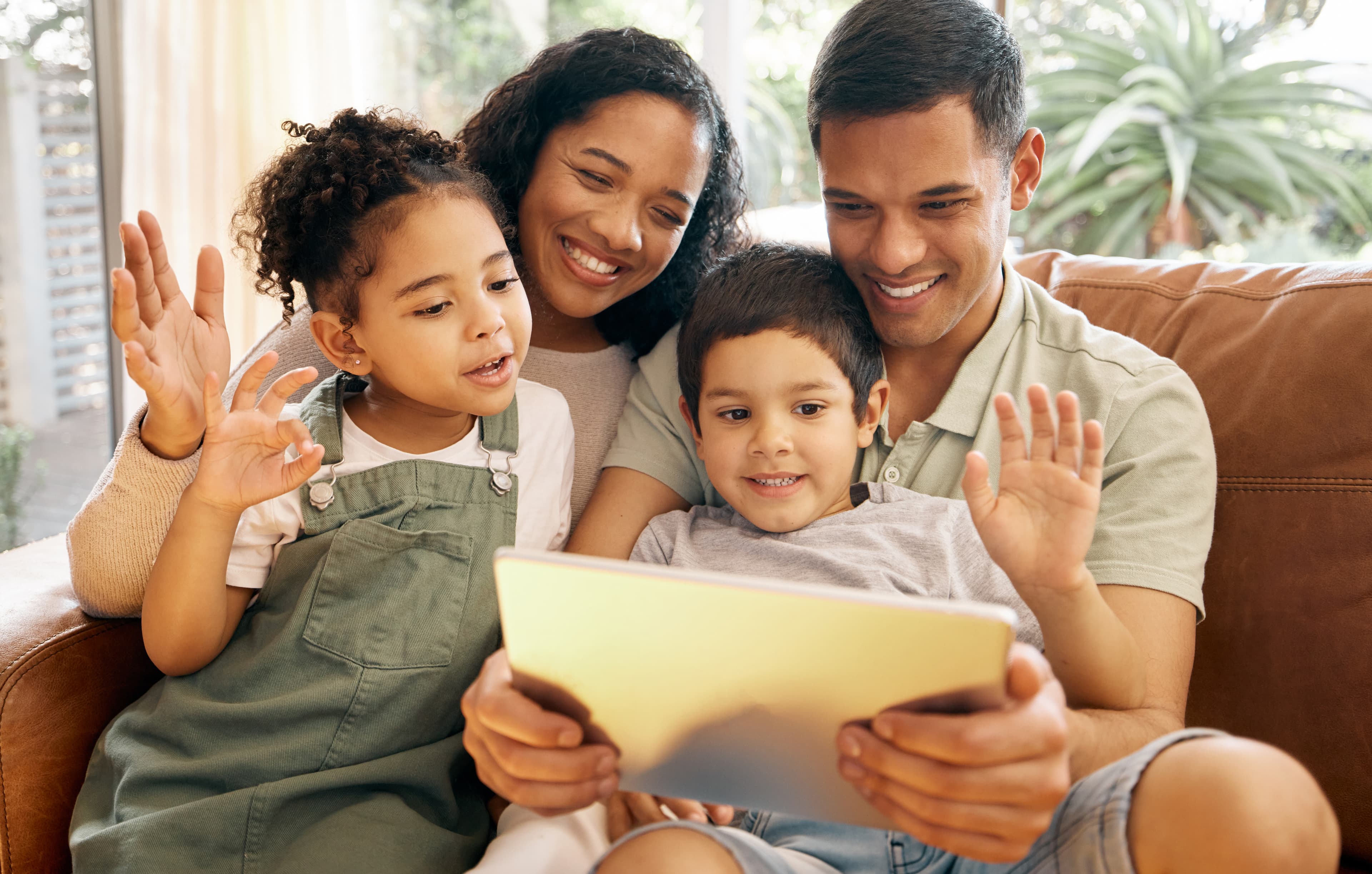 Family gathered on a couch together waving at a tablet